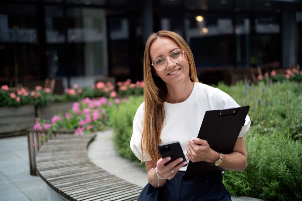 Uśmiechnięta Eliza Hamera z notatnikiem wśród zieleni